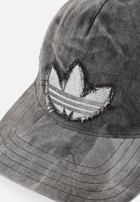 Casquette en tissu gris avec un logo brodé usé représentant trois feuilles et des rayures. Le design comprend des détails de couture visibles.