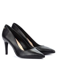 Zapatos de tacón alto de cuero negro con un diseño de punta afilada, tacón stiletto delgado y un detalle de marca minimalista en la parte trasera. Textura suave.