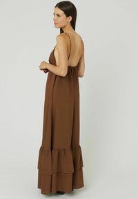 Robe maxi marron avec des fines bretelles, un dos plongeant et un ourlet festonné. Fabriquée en tissu doux, elle présente une coupe ample et une silhouette décontractée.