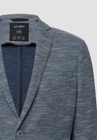 Strukturierter blauer Blazer mit Reverskragen, einem Knopfverschluss und einer Brusttasche. Das Innenfutter besteht aus einem kontrastierenden dunklen Stoff.