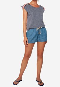 Top gris de manga corta con acentos de hombro estampados, combinado con pantalones cortos de tiro alto de color azul claro con cordones. Sandalias planas completan el look casual.
