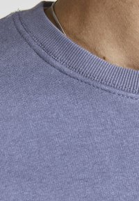 Sudadera de cuello redondo en color gris-púrpura, fabricada con un tejido suave y con textura acanalada, que presenta un escote suave y detalles de costura sutiles.