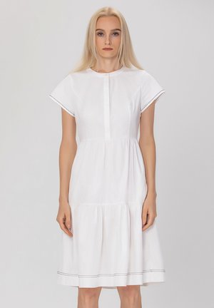 Robe en coton blanc avec des manches courtes, un col rond, une patte de boutonnage et une jupe à volants froncés ; présente des coutures noires discrètes au niveau de l'ourlet.
