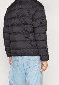 Svart puffy jacka med horisontell sömnad, med rundad halsringning och långa ärmar. Bärs med ljusblå löst sittande jeans.