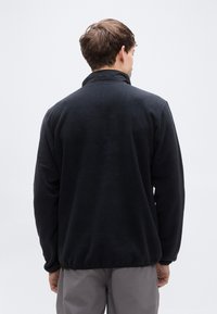 Μαύρο φλις πουλόβερ με ψηλό γιακά, χαρακτηρισμένο από ομαλή υφή και ελαστικές μανσέτες. Άτυπο σχέδιο με απλή, καθαρή σιλουέτα.