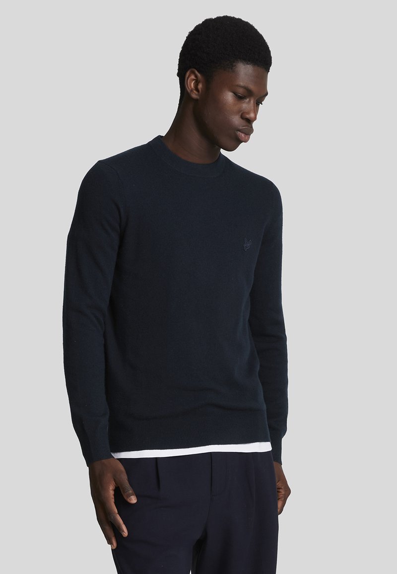 Marinblå stickad tröja med rund hals, långa ärmar och ribbad nederkant. Har en diskret logotyp på bröstet och en mjuk textur.