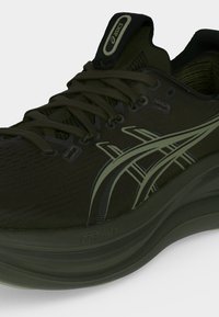 Σκούρο ελιάς πράσινο αθλητικό παπούτσι ASICS με δέσιμο, επάνω μέρος από δίχτυ και ανοιχτό πράσινο λογότυπο στο πλάι.