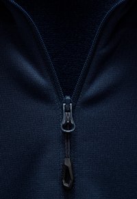 Marinblå zip-up jacka med en närbild av en dragkedja, som har en texturerad tyg och en dragflik med svarta detaljer.