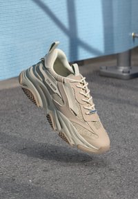 Beige mesh sneaker with a chunky design, textured accents, and light blue laces. Branding "Steve Madden" visible on the side.