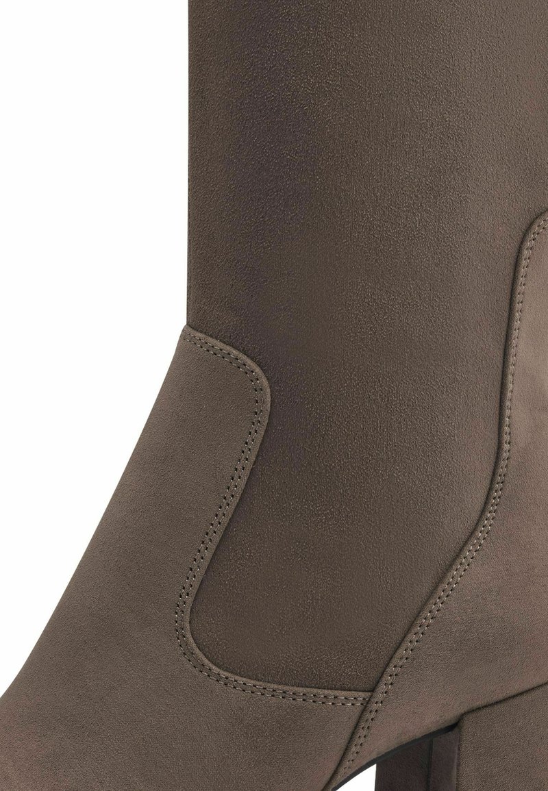 Nahaufnahme eines taupefarbenen Wildleder-Stiefeletten mit genähtem Paneeldetail und Blockabsatz.