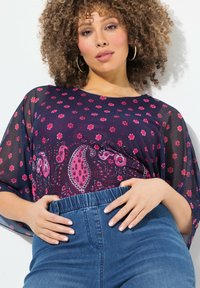 Kuvioitu, läpinäkyvä tummansininen toppi, jossa on leveät hihat, yhdistettynä korkeavyötäröisiin sinisiin farkkuihin. Sisältää vaaleanpunaisia paisley- ja kukkakuoseja.