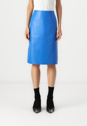 Blauwe leren pencilrok met een gladde textuur, knielange snit en minimale naden. Gecombineerd met zwarte sokken en schoenen met hak.