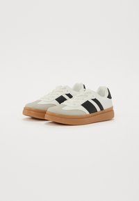 Adidași albaștri și negri, cu vârful din suede gri deschis, talpă din cauciuc de tip gumă și trei dungi negre pe părți. Sforile sunt albe.