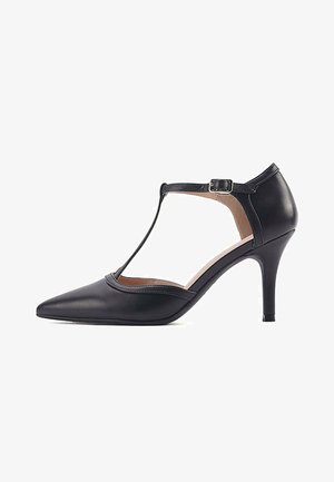 Scarpa con tacco alto in pelle nera, con punta a punta, design a T e cinturino regolabile alla caviglia. Texture liscia e silhouette elegante.