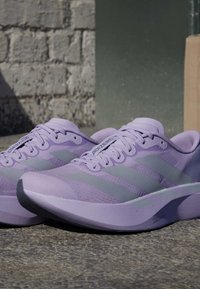 Para jasnofioletowych sportowych butów do biegania z szarymi paskami i logo "Adizero", umieszczona na teksturowanej powierzchni zewnętrznej.