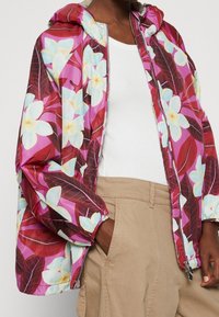 Floral windbreaker featuring a vibrant pink and burgundy pattern, with a hood, elastic cuffs, and a zipper closure. Lightweight fabric.