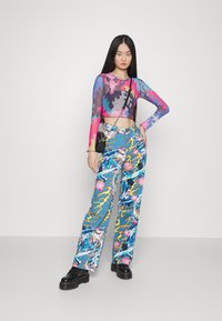 Top cropped de manga longa com estampa abstrata multicolorida; calças largas azuis com padrões vibrantes; modelo a usar sapatos plataforma pretos.