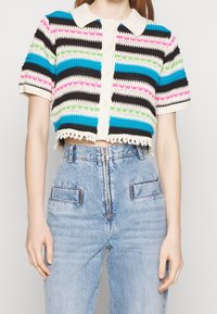 Virkat kort topp med en krämfärgad krage. Har horisontella ränder i blått, svart, rosa och grönt, med en texturerad yta och fransat avslut.