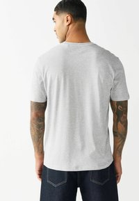Grå kortærmet t-shirt med ribbet rund hals. Har en glat tekstur og en afslappet pasform. Bæres med mørke denimjeans.