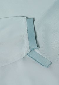 Helles blaues Gewebe mit einer glatten Textur, das mit einem gerafften Bund und einem kontrastierenden Gummiband in einem etwas dunkleren Blau versehen ist.