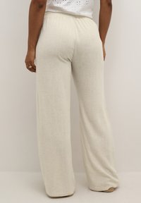 Pantaloni largi bej deschis, cu un talie elastică, textură moale a materialului și un design minimalist, prezentați din spate.