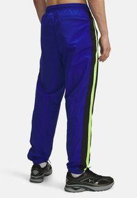 Heren joggers in felblauwe stof met zwarte en neon groene zijstrepen, voorzien van een elastische tailleband en taps toelopende boorden.