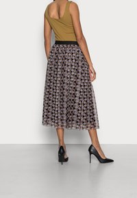 Débardeur vert associé à une taille élastique noire, jupe midi superposée avec un imprimé géométrique dans des tons doux, et chaussures à talons noirs.