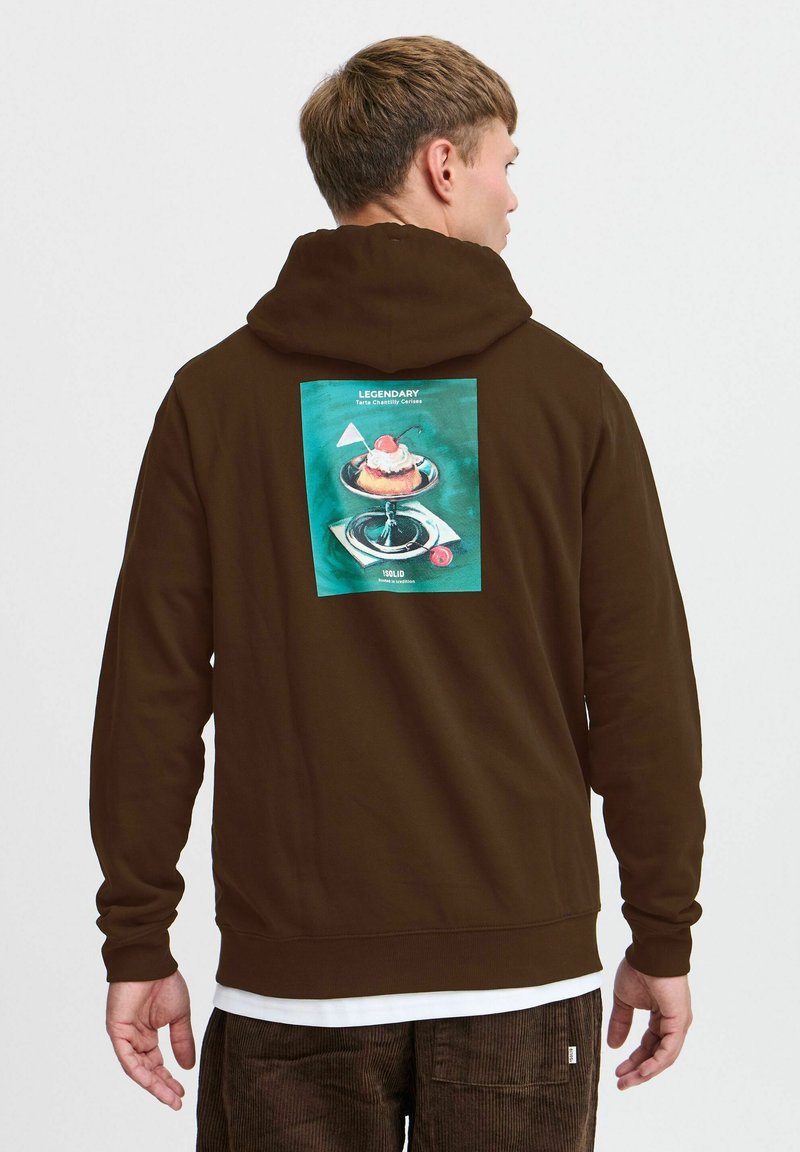 Brun hættebluse med stort grafisk print på ryggen, der viser en dessert på en glasstand, sat mod en teal baggrund. Blød tekstur, afslappet pasform.