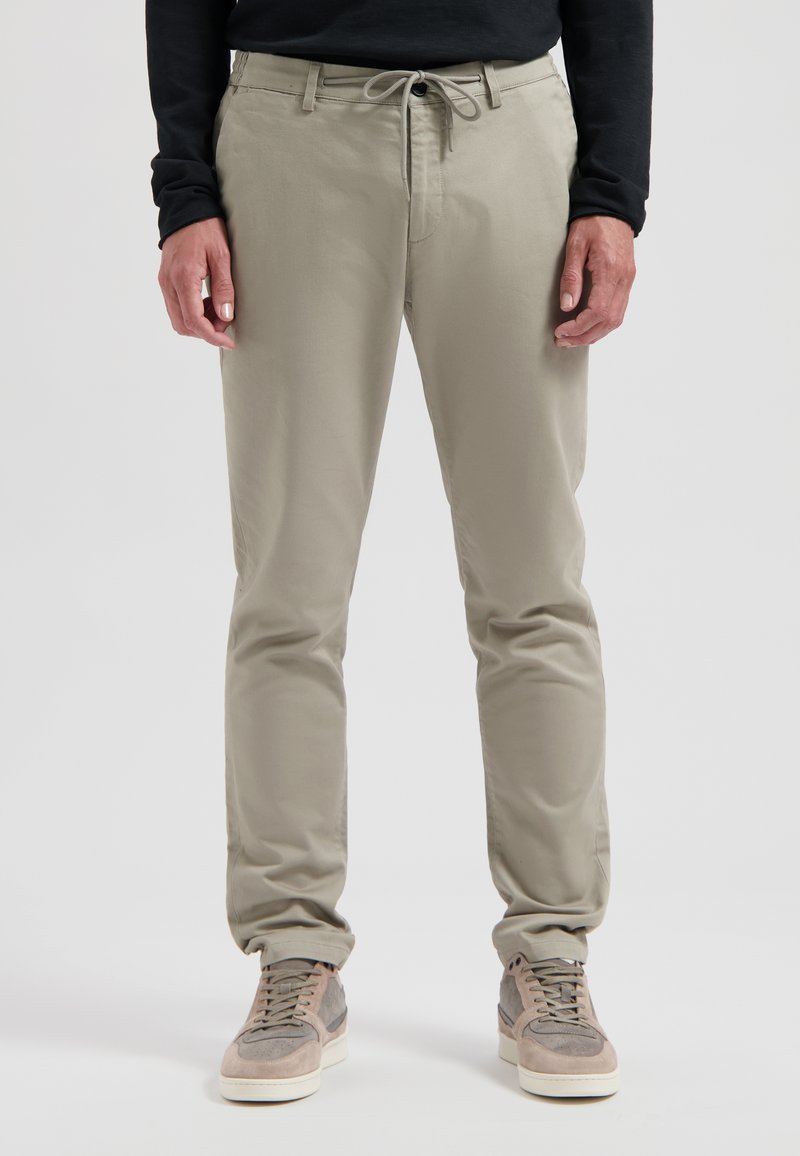 Pantaloni tapered grigi chiari con vita regolabile, tasche laterali e tessuto morbido. Abbinati a sneakers grigie chiare e beige.