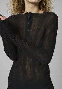 Čierny rebrovaný vrchný diel s dlhým rukávom a polopriehľadnou textúrou, featuring okrúhly výstrih, zapínanie na tri gombíky a priliehavý strih.