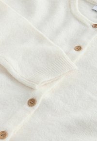 White knit cardigan with a soft texture, featuring a button-down front, ribbed cuffs, and wooden buttons for added detail.