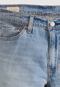 Jeans in denim azzurro chiaro con una finitura slavata, dotati di chiusura lampo, bottone in metallo e dettagli di cucitura arancione.