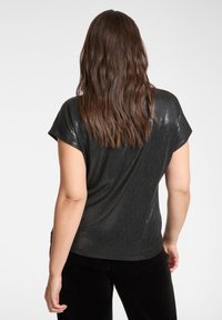 Svart topp med korta ärmar och glänsande, texturerad yta. Har en avslappnad passform och rundad nederkant, kombinerad med svarta byxor.