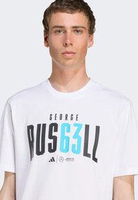 White t-shirt featuring bold black and blue text "GEORGE RUS63LL" and logos. Soft fabric, relaxed fit, crew neckline, short sleeves.