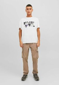 Camiseta blanca con texto gráfico multicolor en el centro. Pantalones cargo beige con bolsillos laterales. Zapatos oscuros con una superficie texturizada.
