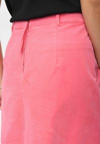 Rosa tygshorts med en mjuk textur, featuring dragkedjestängning och sidofickor. Designen är enkel och skräddarsydd för komfort.
