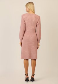 Rosa gestricktes Kleid mit strukturiertem Rippmuster, Ballonärmeln und Zopfmuster-Details auf der Rückseite. Knie-länglich mit taillierter Silhouette.