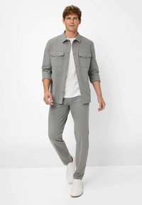 Camicia grigia con bottoni, dotata di due tasche sul petto, abbinata a pantaloni slim-fit coordinati e sneakers bianche. Tessuto liscio, design casual.
