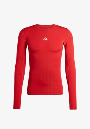 T-shirt de compression athlétique rouge à manches longues avec col rond et petit logo Adidas blanc centré sur la poitrine.