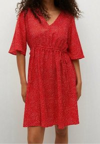 Robe rouge à manches courtes avec un décolleté en V, dotée d'une taille cintrée, d'une coupe ample et de petits pois blancs sur un tissu texturé.