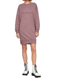 Violet oversize-mekko pitkillä hihoilla ja pyöreällä kaula-aukolla, jossa on kohokuvioitu "la femme" -kuvaus. Yhdistettynä valkoisiin nauhakengiin.