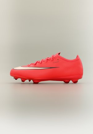 Crampon de football rouge vif avec swoosh noir et blanc, design bas, lacets et crampons moulés pour jouer sur terrain ferme.