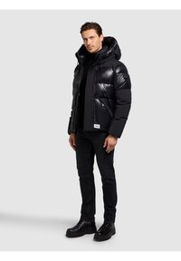 Črno puhovko s sijočim, prešitim videzom, kapuco in sprednjimi žepi. Oblečena čez črno majico, kombinirano s temnimi kavbojkami in črnimi škornji.