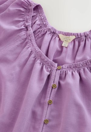 Lavender linen top with a round neckline, gathered detailing, and wooden buttons down the front. Soft texture and lightweight fabric.