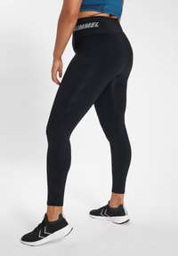 Svarta sportleggings med en texturerad design och hög midja som har "Hummel"-logotypen. Kombinerat med svarta och vita sneakers.