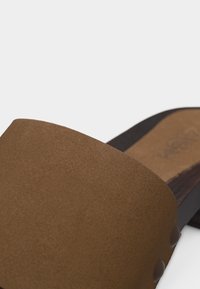 Chaussure à enfiler en daim marron avec large bride supérieure et semelle intérieure moulée sur fond blanc.