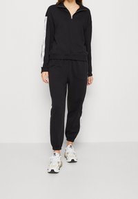 Svart sweatshirt med zipkrage och sidostripes, i kombination med svarta joggers med vita detaljer. Bärs tillsammans med sportiga sneakers.