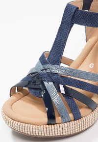 Sandale bleue pour femme avec un mélange de lanières texturées et brillantes et une semelle intérieure beige rembourrée sur le bord de la semelle tissée.