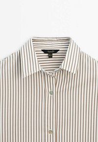 Randig skjorta med knappar som har smala bruna och vita vertikala ränder, en spetsig krage och en enda knappstängning framtill.