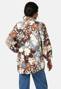 Floral patterned shirt in brown, cream, and blue. Lightweight fabric, long sleeves, loose fit, featuring large flowers and accent details.